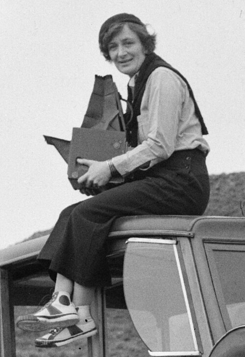 Portrait of documentary photographer Dorothea Lange atop a car with her large camera.